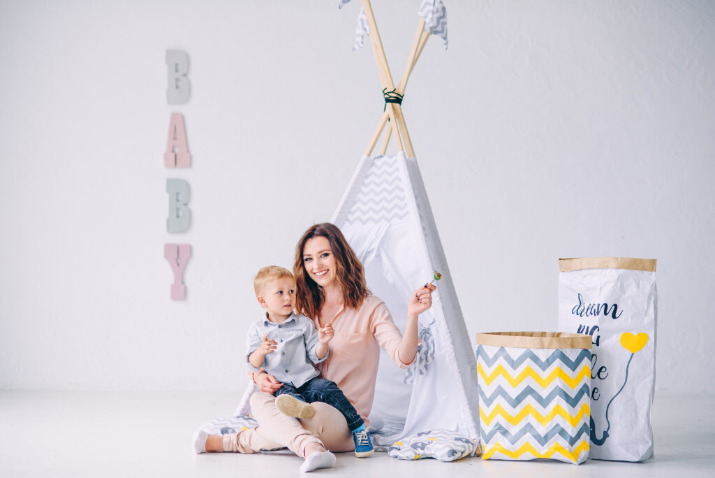beautiful-young-mother-gives-candy-her-little-son-light-room-with-children-s-wigwam-eco-bags-toys