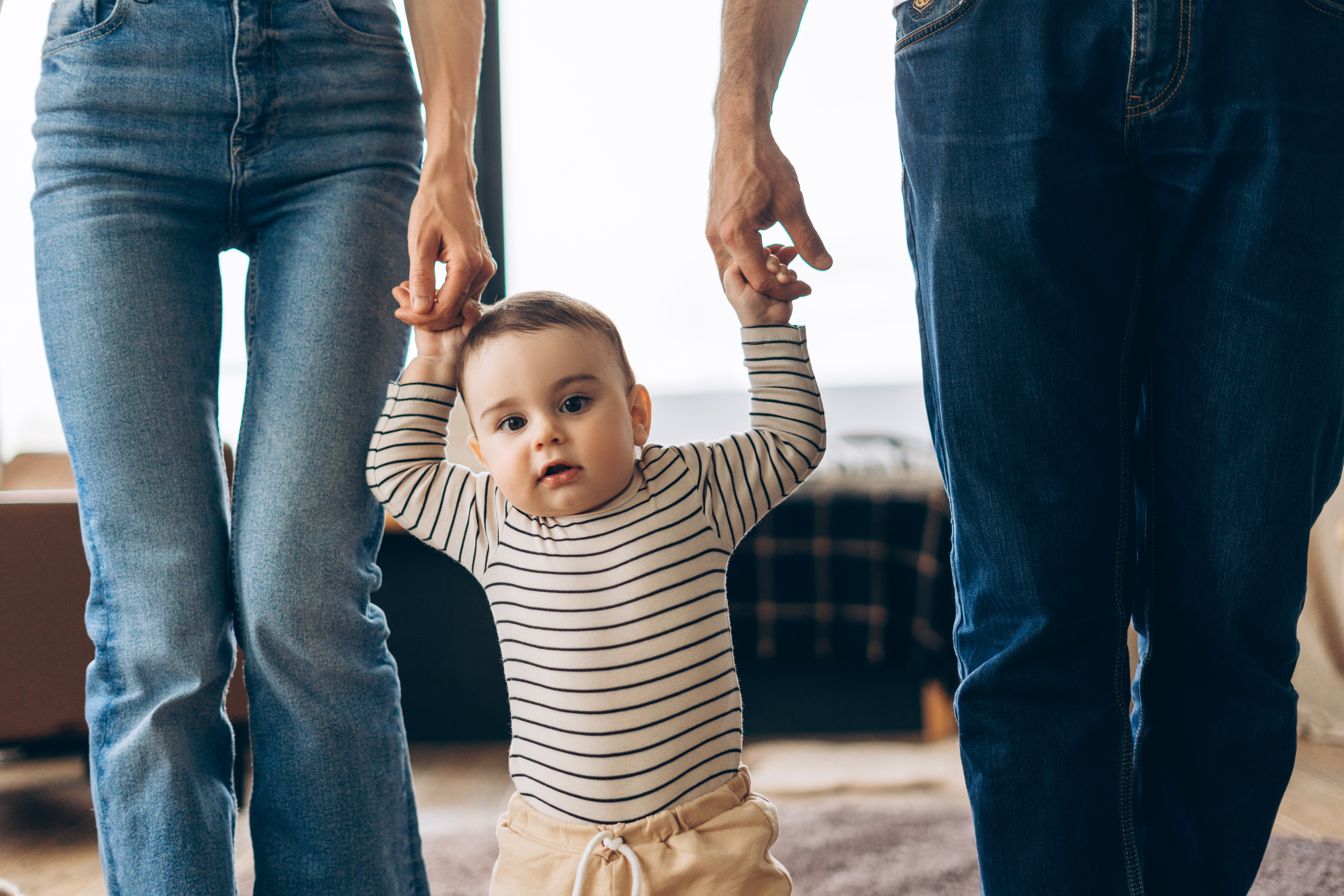 Happy baby boy learning to walk holding parents hands