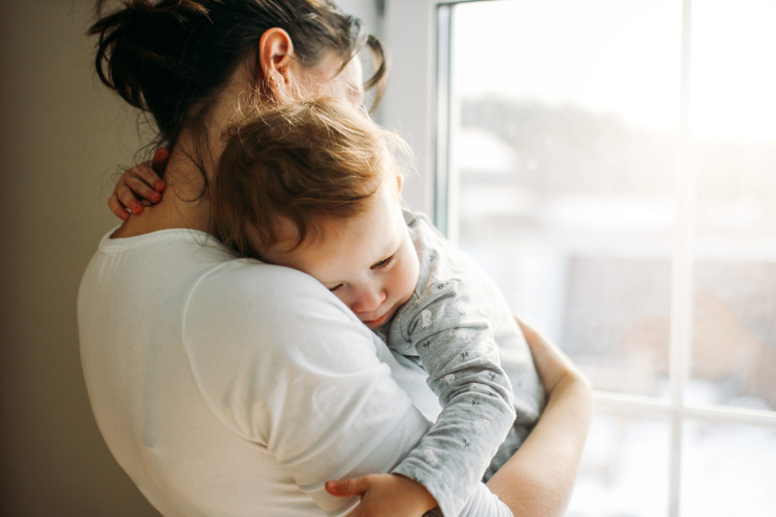 Young woman mom with baby girl on hands near window at home