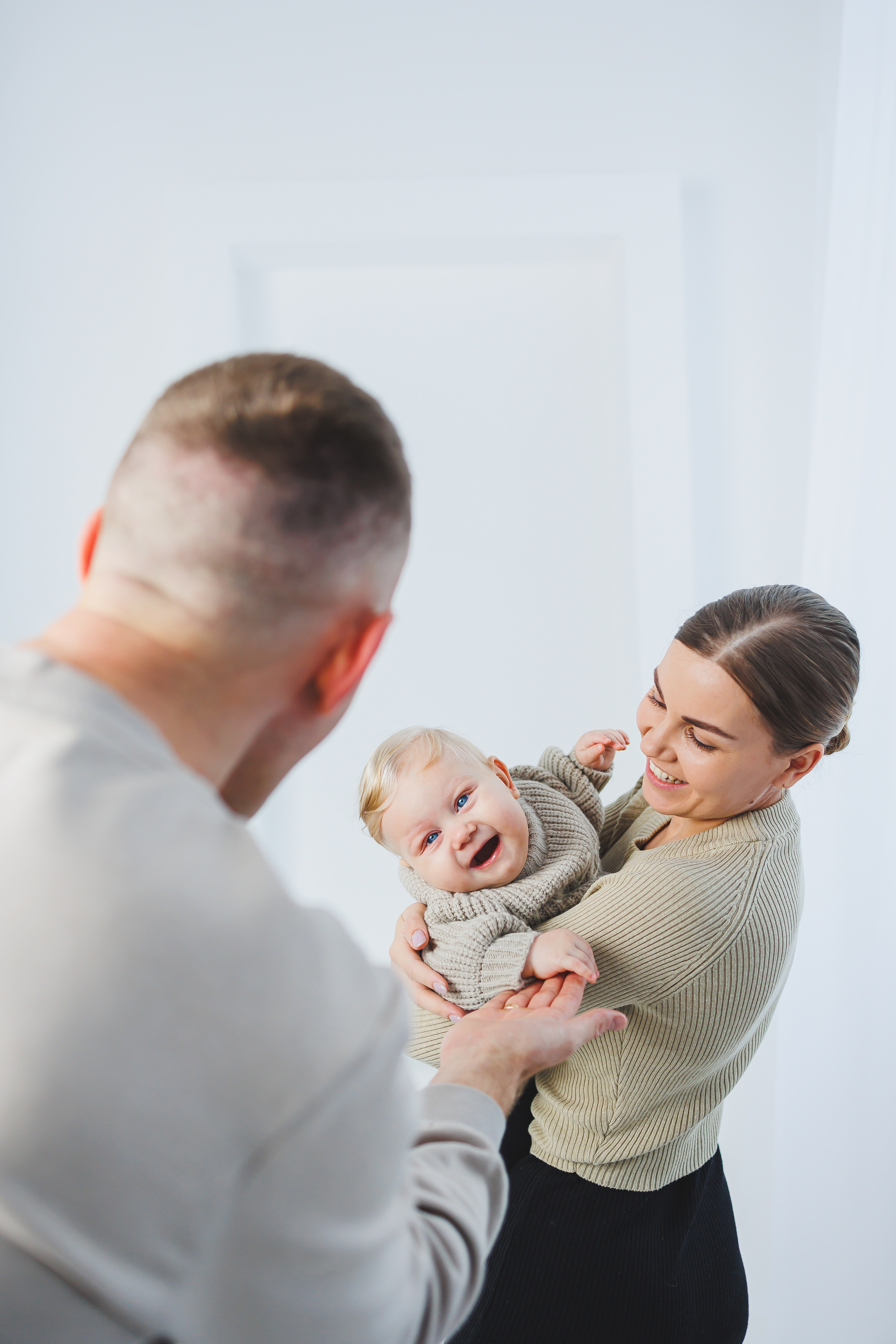 Young parents mom and dad are playing with a baby on a white background. A married couple hugs their newborn son. A happy family.
