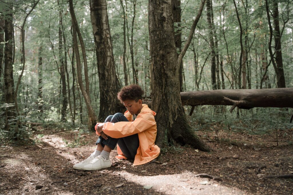 A young boy in a bright jacket sits alone in a forest